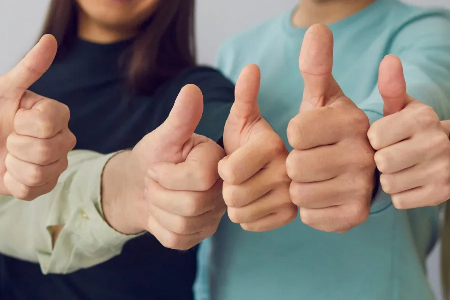 Close-up of five diverse people giving a thumbs-up gesture, with a focus on their hands in the foreground.