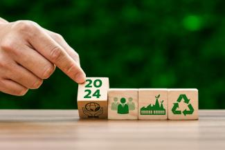 Una mano alineando piezas de madera con símbolos de sostenibilidad.